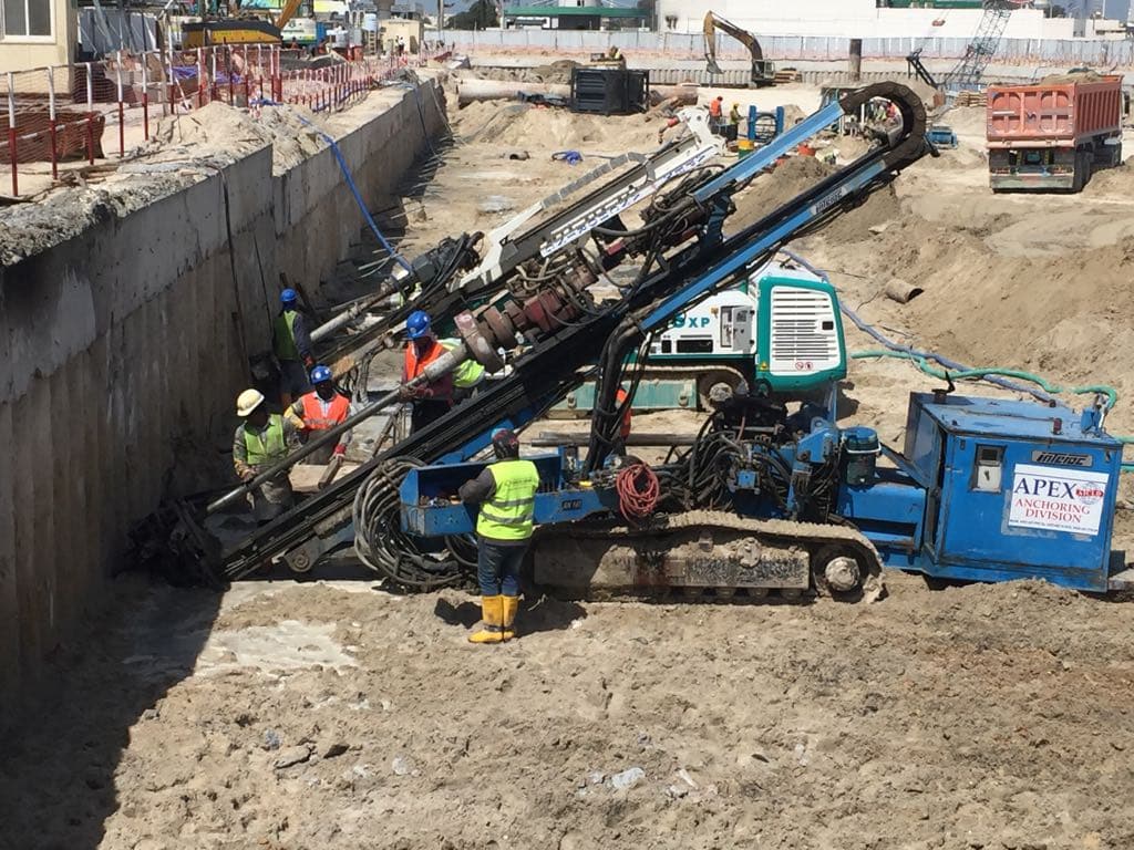 Apex Anchoring Division rig drilling a tie-back anchor on rake into a shored excavation wall in the UAE